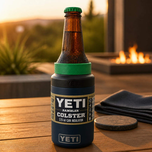A Coopers Original Pale Ale bottle fitted with a green TOPA FitSeal adapter insert, sitting securely in a navy YETI Rambler Colster 375ml can insulator on a timber outdoor table with a fireplace in the background