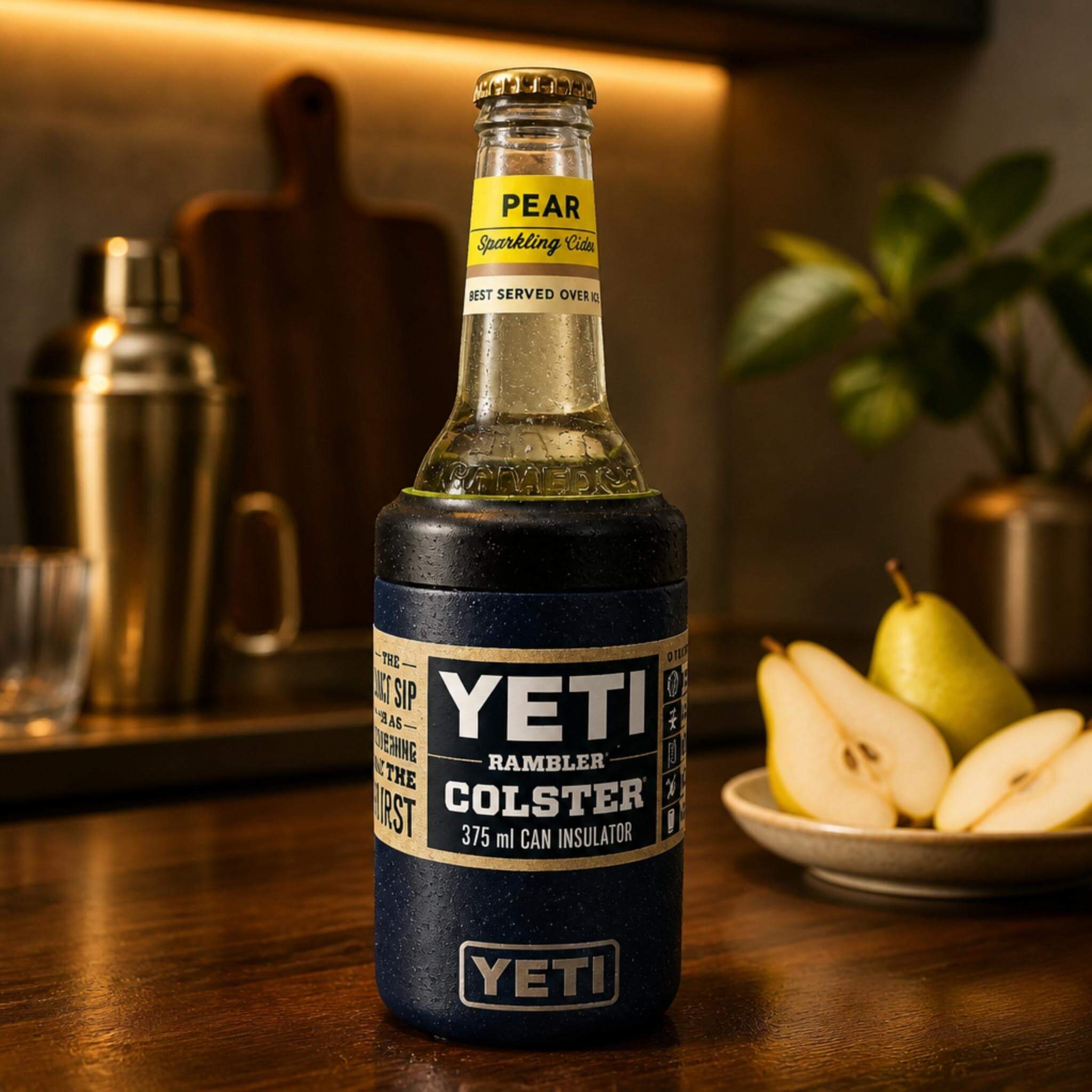 A Somersby Pear Sparkling Cider bottle fitted with a green TOPA FitSeal adapter insert, sitting securely in a navy YETI Rambler Colster 375ml can insulator on a timber bar counter, with sliced pears and bar accessories in the background.